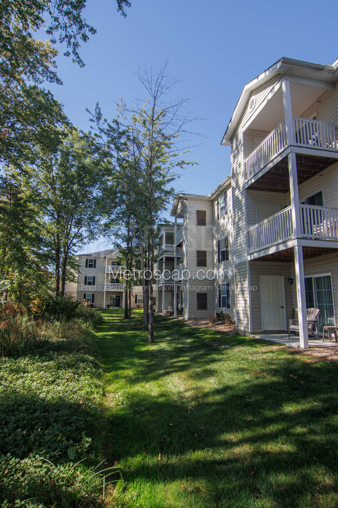 A view of the apartment complex facade with mature trees and a sunny sky